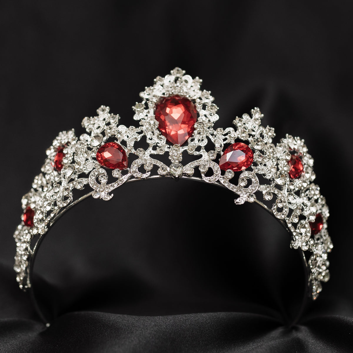 A tiara adorned with silver white gold colored sparkles and large marquise shaped red crystals. bottom view