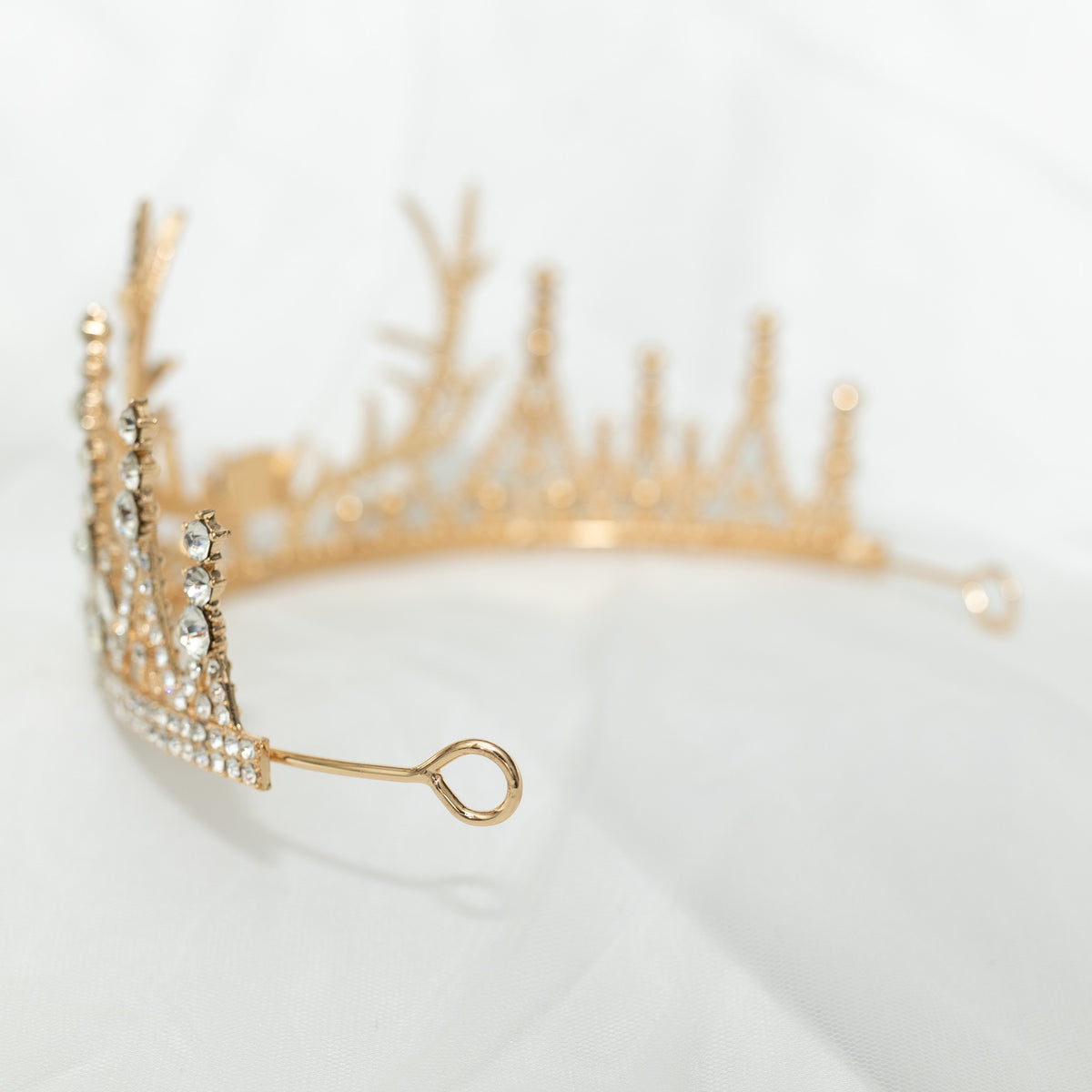 A sparkling tiara with a central red crystal, surrounded by clear crystals on a gold-colored base, designed to resemble antlers, set against a white background. - looped end
