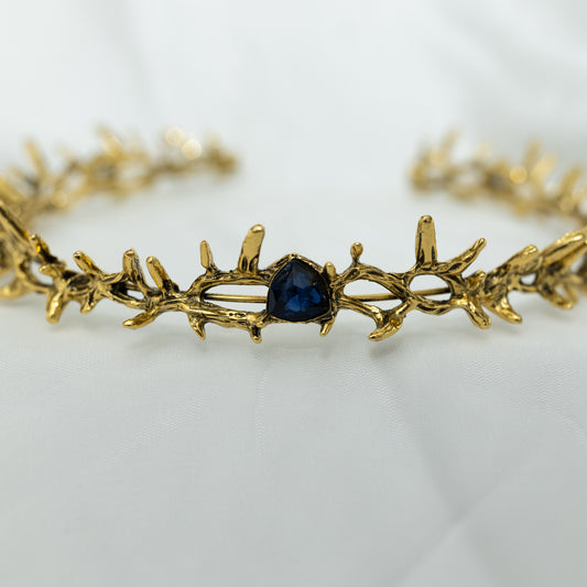 A antique gold colored metal crown with spikes and blue faux sapphire stones.