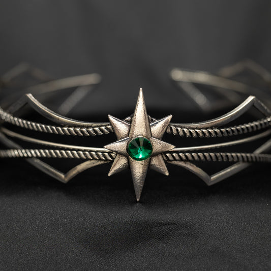 Silver headpiece with a green gemstone on a dark background