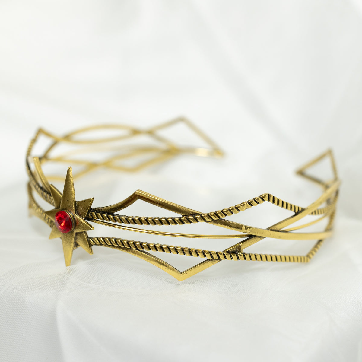 Gold bracelet with geometric design and red gemstone on a white background