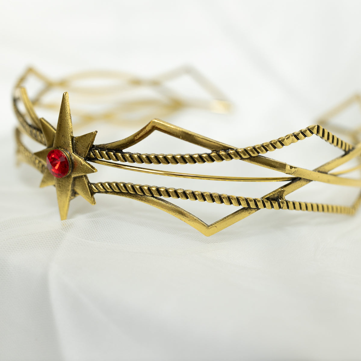 Gold bracelet with star design and red gemstone on a white background
