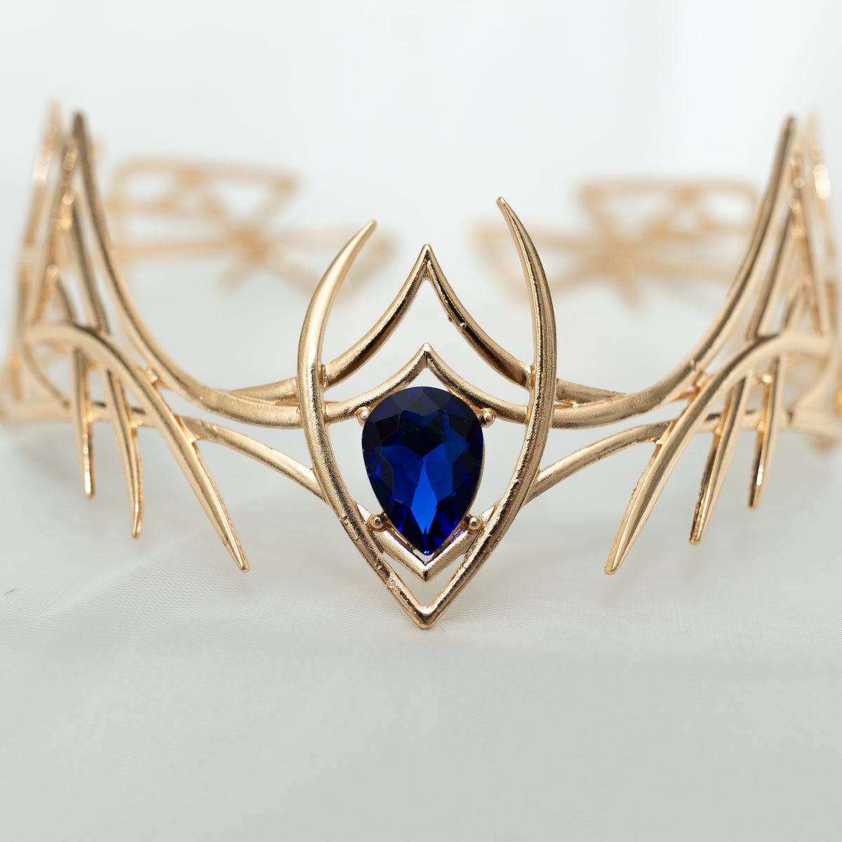 Gold elven-style crown with a blue gemstone on a light gray background