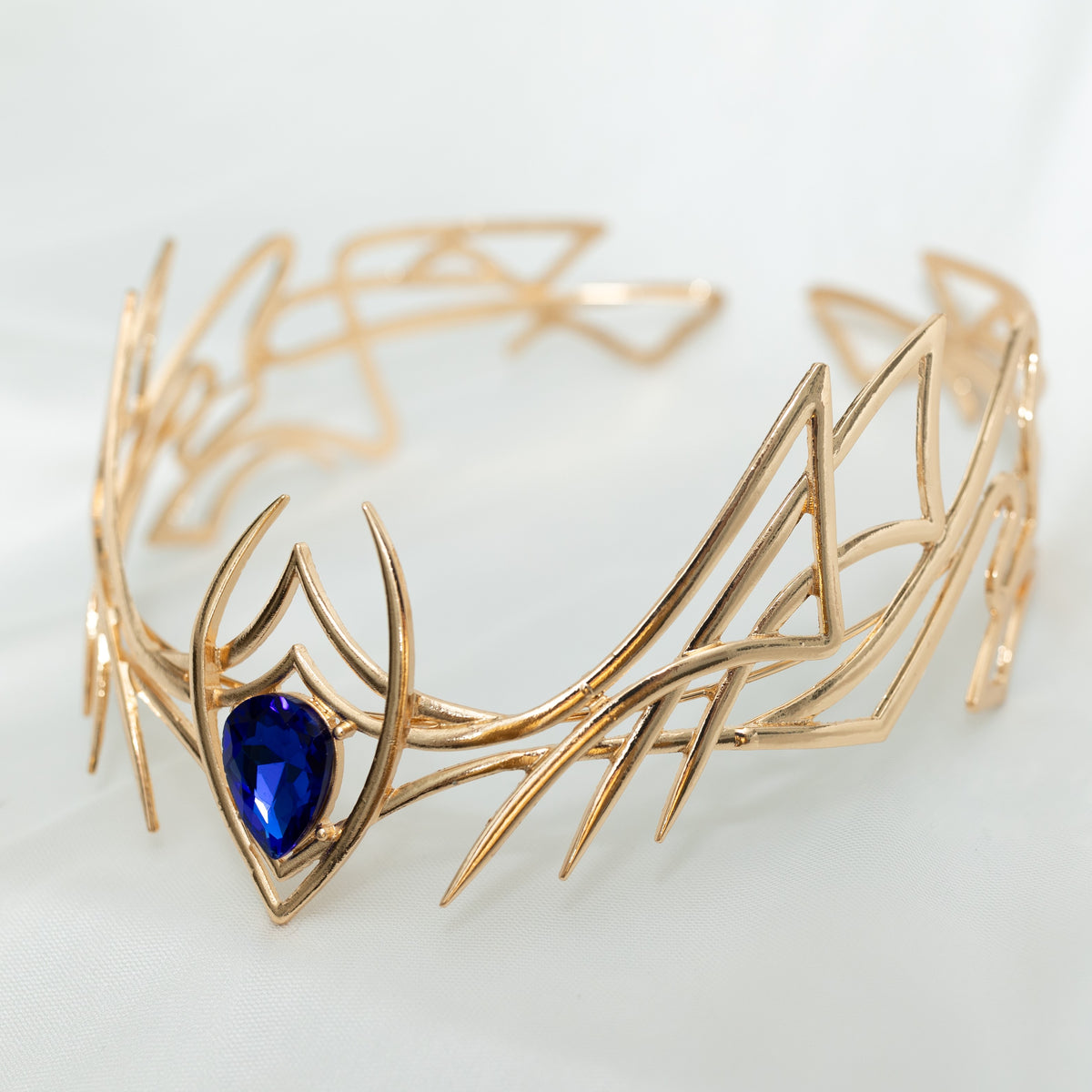 Gold leaf-shaped bracelet with a blue gemstone on a light gray background