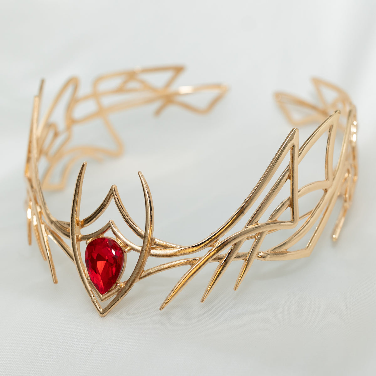Gold leaf-like bracelet with a red gemstone on a light gray background