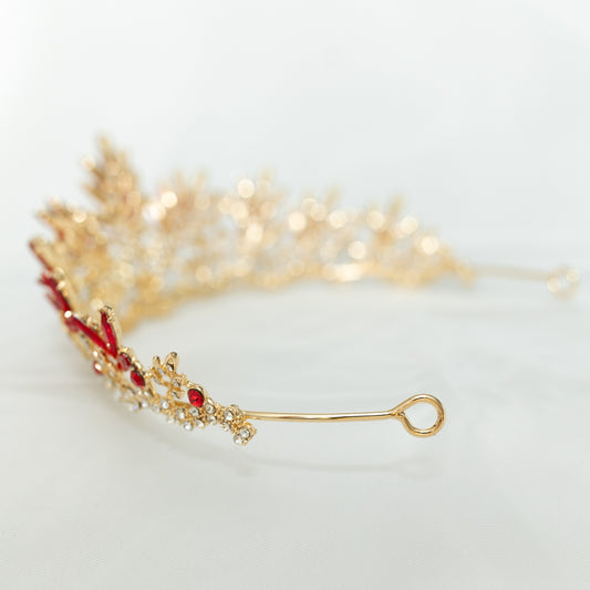 A golden tiara adorned with sharp spikes of red colored crystals against a white background. End view