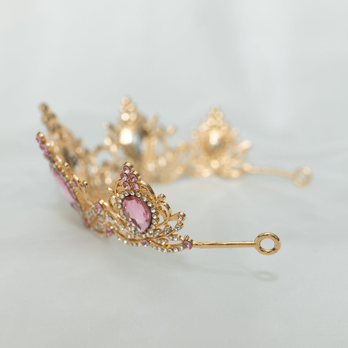 Gold tiara with pink gemstones on a light gray background