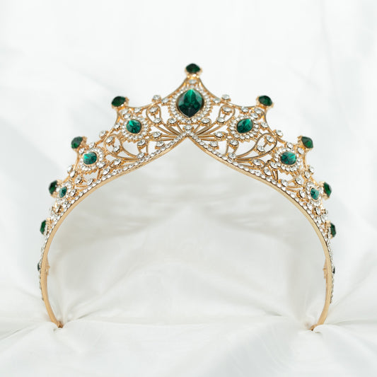 A golden tiara adorned with large green marquise shaped crystals and small clear round crystals, set against a white background. Bottom view