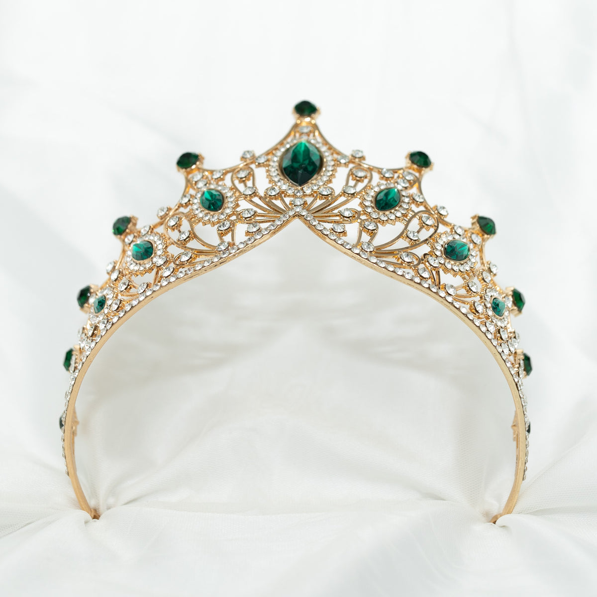 A golden tiara adorned with large green marquise shaped crystals and small clear round crystals, set against a white background. Bottom view