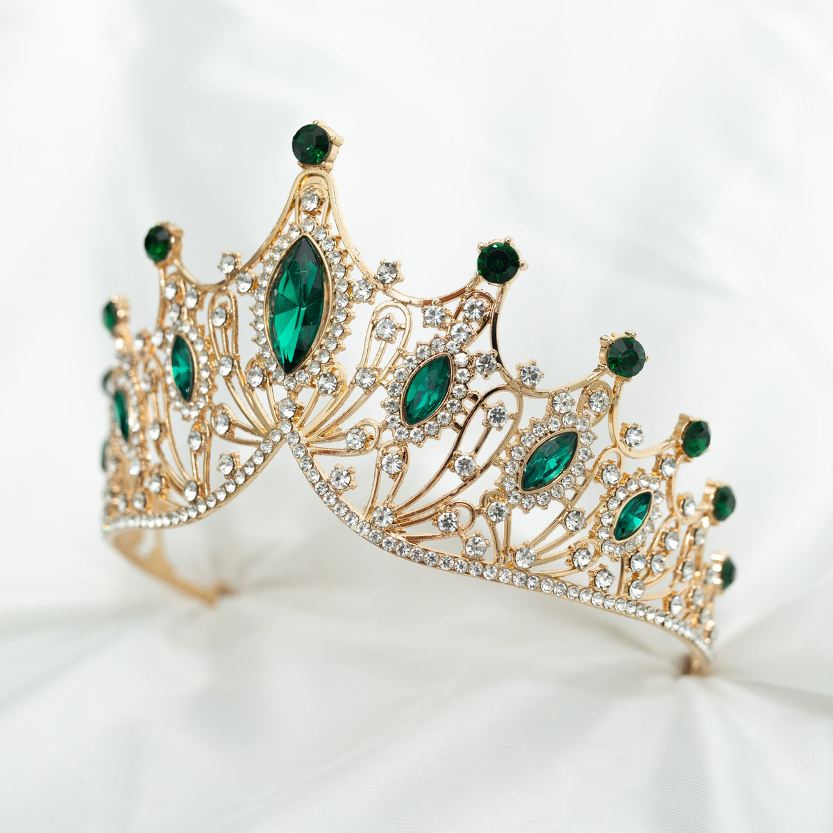 A golden tiara adorned with large green marquise shaped crystals and small clear round crystals, set against a white background. Front side view