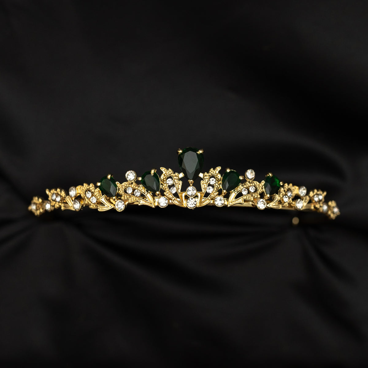 Gold tiara with green stones on a black fabric background