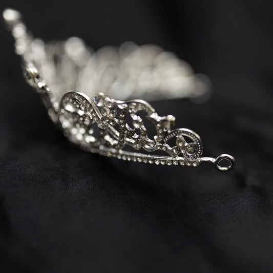 Elegant silver crystal tiara with intricate scrollwork design and sparkling rhinestones, photographed on a black background - End Side View