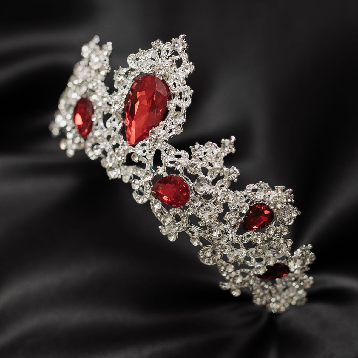 A tiara adorned with silver white gold colored sparkles and large marquise shaped red crystals. front angle view