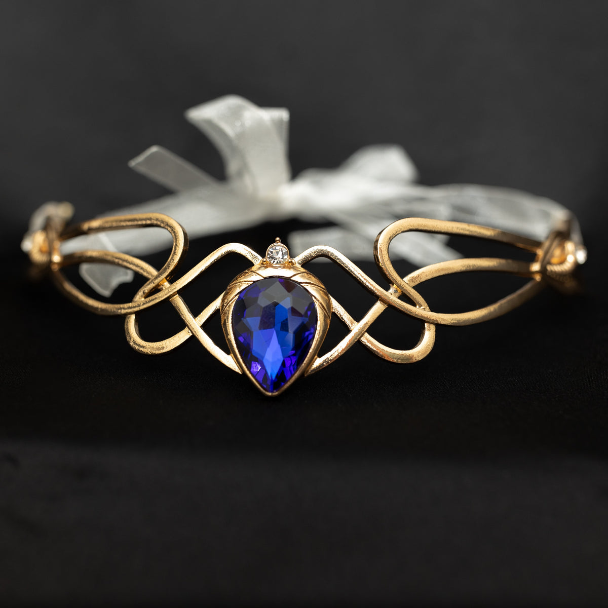 Gold bracelet with a blue heart-shaped gemstone on a dark background