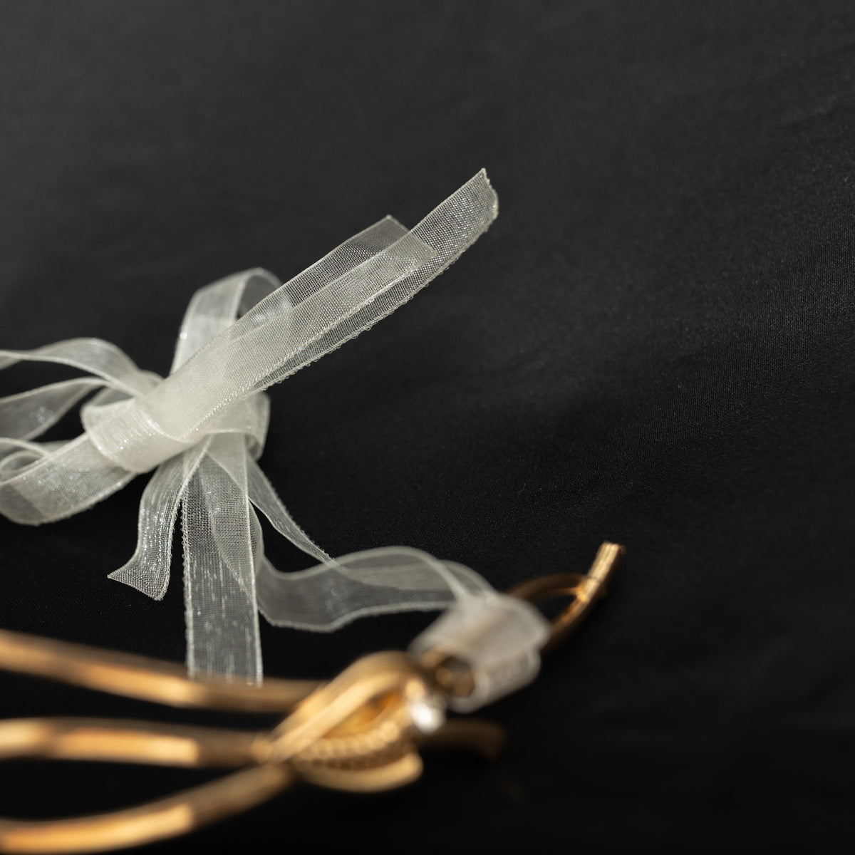 Gold bracelet with a white ribbon on a black background