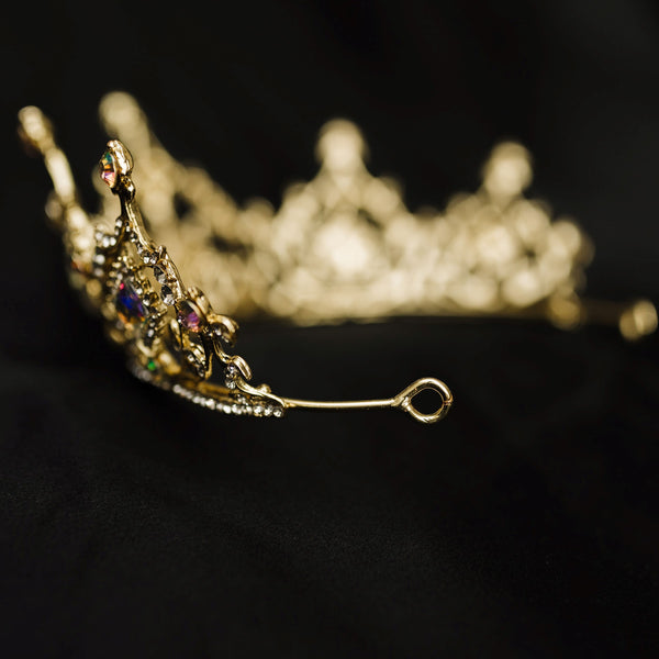 Gold tiara with opal glass crystal gemstones on a black fabric background_ Looped End
