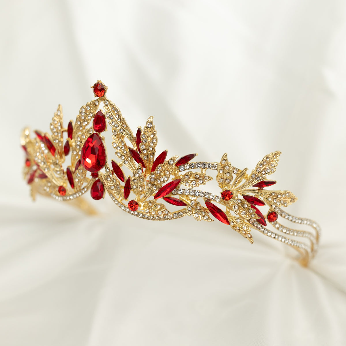 A golden tiara with red crystal embellishments and leaf detailing, displayed against a white background. - Front Angle View