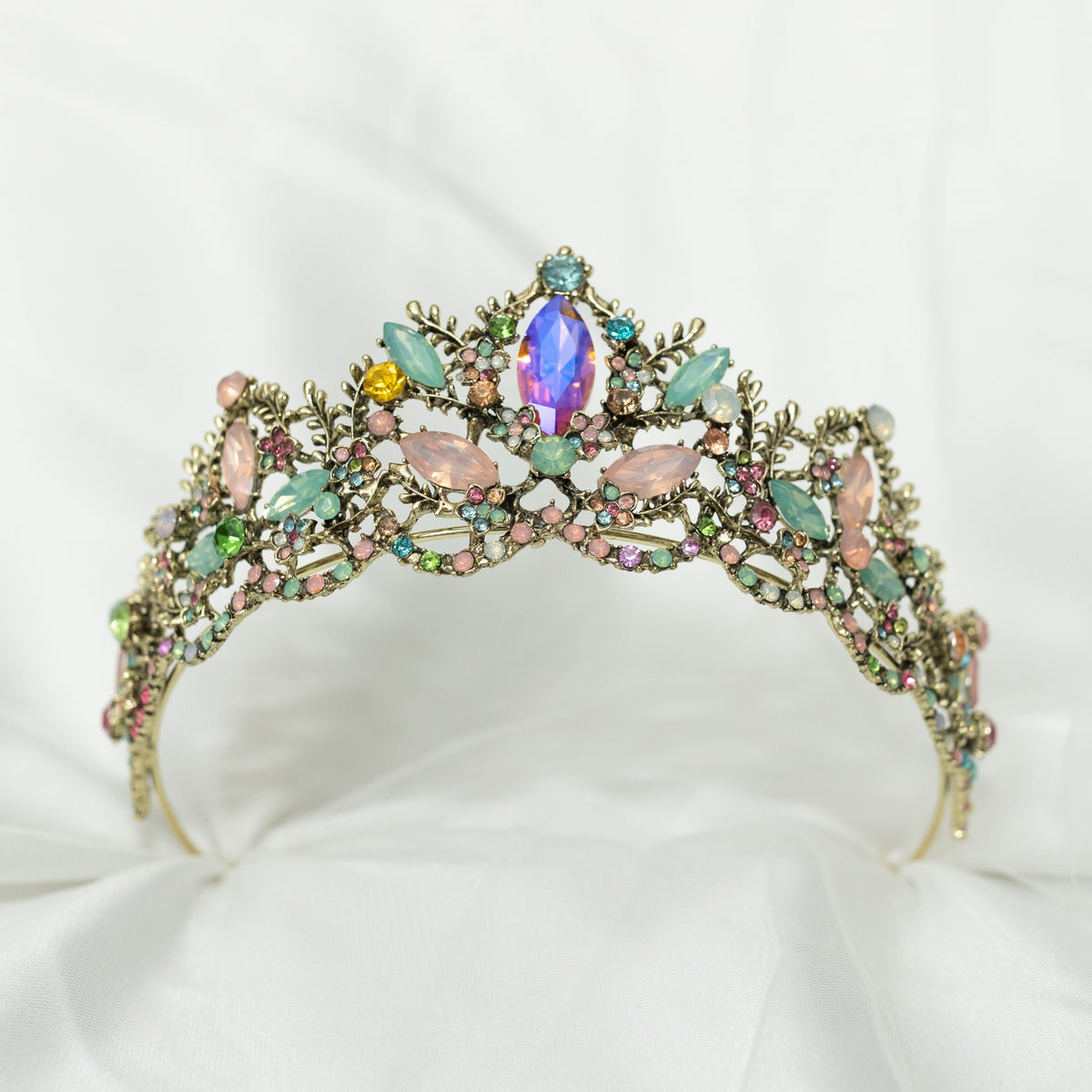 An antique gold-colored tiara adorned with large blue and pink crystals, and accented with pink, peach, blue, and turquoise color crystals. bottom front