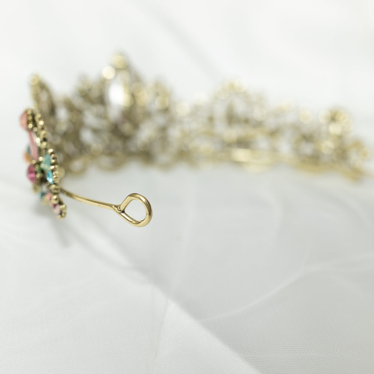 An antique gold-colored tiara adorned with large blue and pink crystals, and accented with pink, peach, blue, and turquoise color crystals. looped end