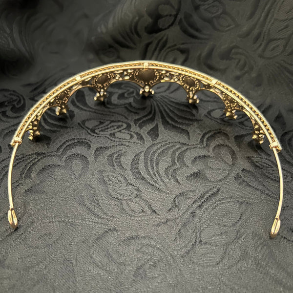 A gold filigree crown tiara with delicate hanging beads, displayed on a textured black damask fabric background.