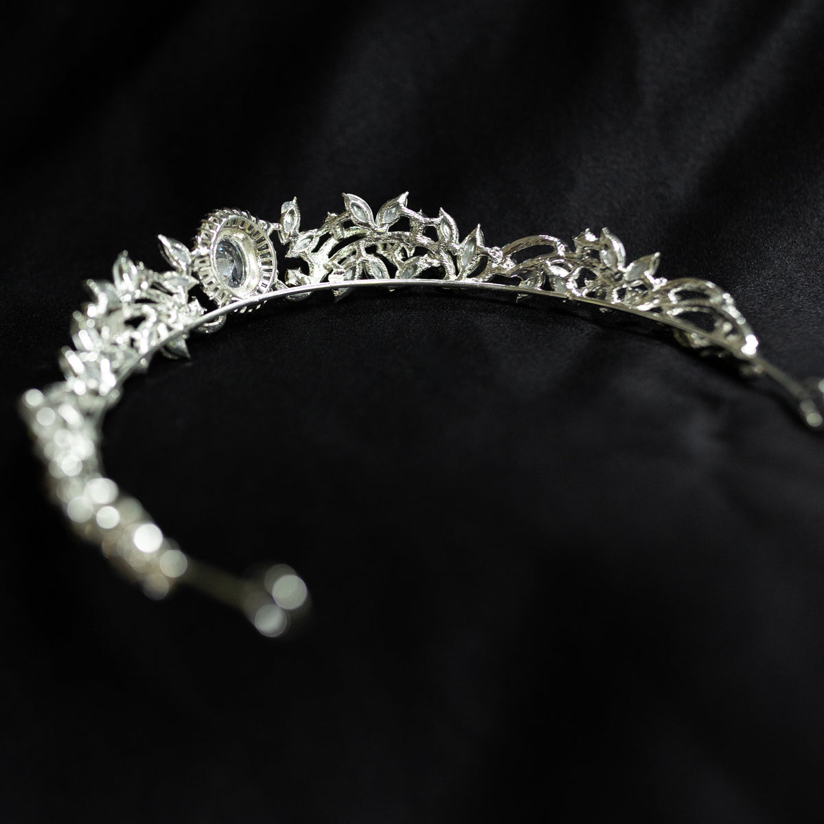 A silver-colored tiara with a central oval-shaped clear crystal surrounded by a halo of smaller baguette-style crystals, designed for hair adornment. back