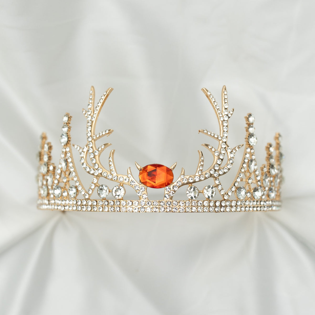 A sparkling tiara with a central red crystal, surrounded by clear crystals on a gold-colored base, designed to resemble antlers, set against a white background.
