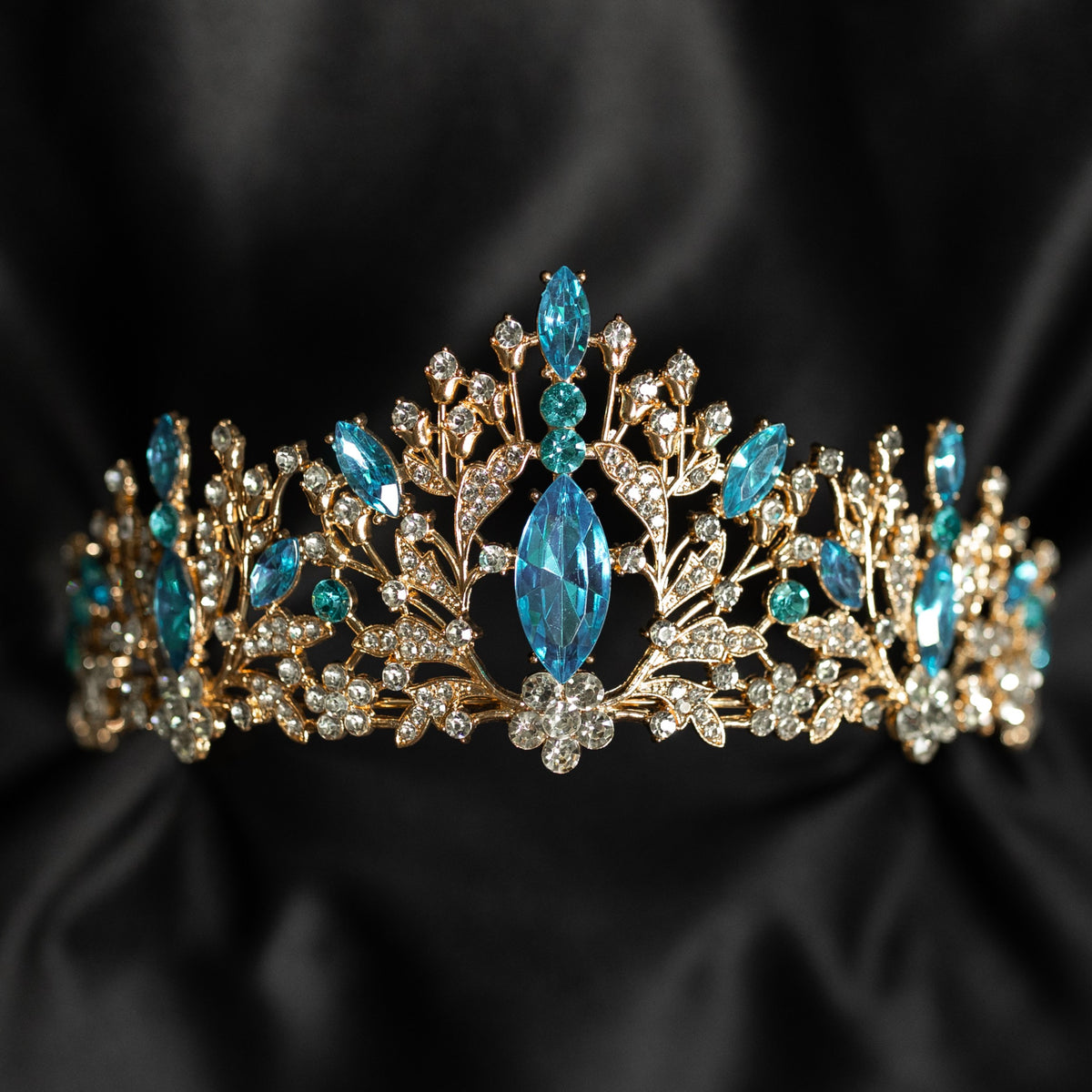 Felicity's Tiara in Light Blue & Gold - A light blue and gold tiara with floral patterns and aqua aquamarine turquoise crystals set in gold-colored metal, displayed against a black background - Front View 