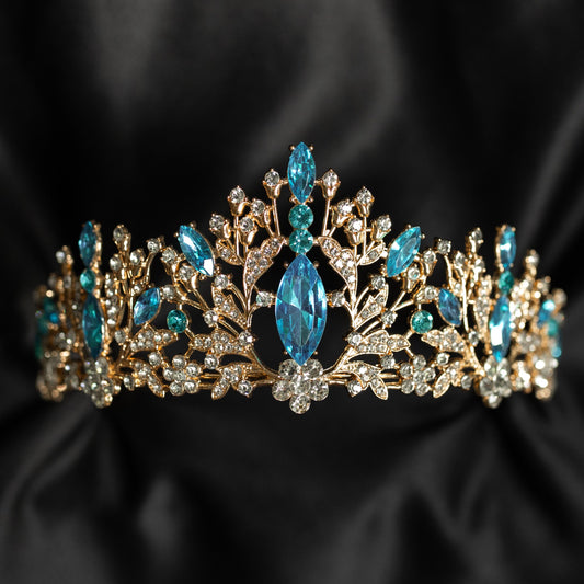 Felicity's Tiara in Light Blue & Gold - A light blue and gold tiara with floral patterns and aqua aquamarine turquoise crystals set in gold-colored metal, displayed against a black background - Front View 
