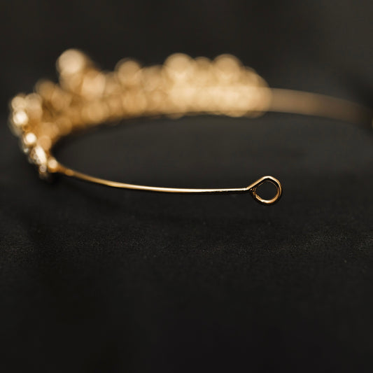 A gold-colored metal tiara with clear crystal embellishments, displayed against a black background. looped end 