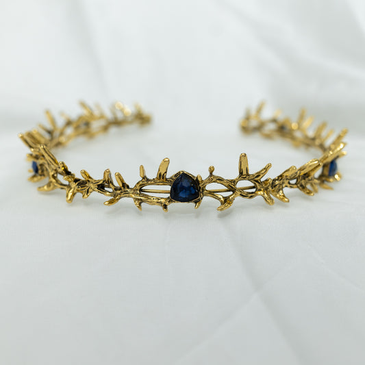 A antique gold colored metal crown with spikes and blue faux sapphire stones.