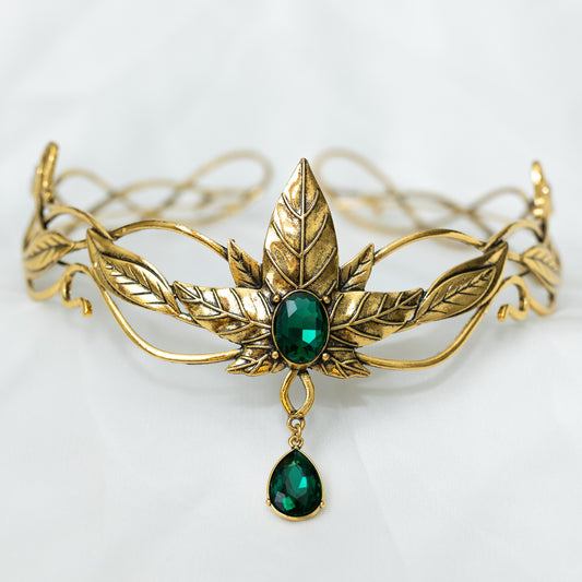 A golden tiara featuring a central green crystal with additional leaf detailing and a dangling green crystal, designed for adult cosplay or as a decorative piece. Front view