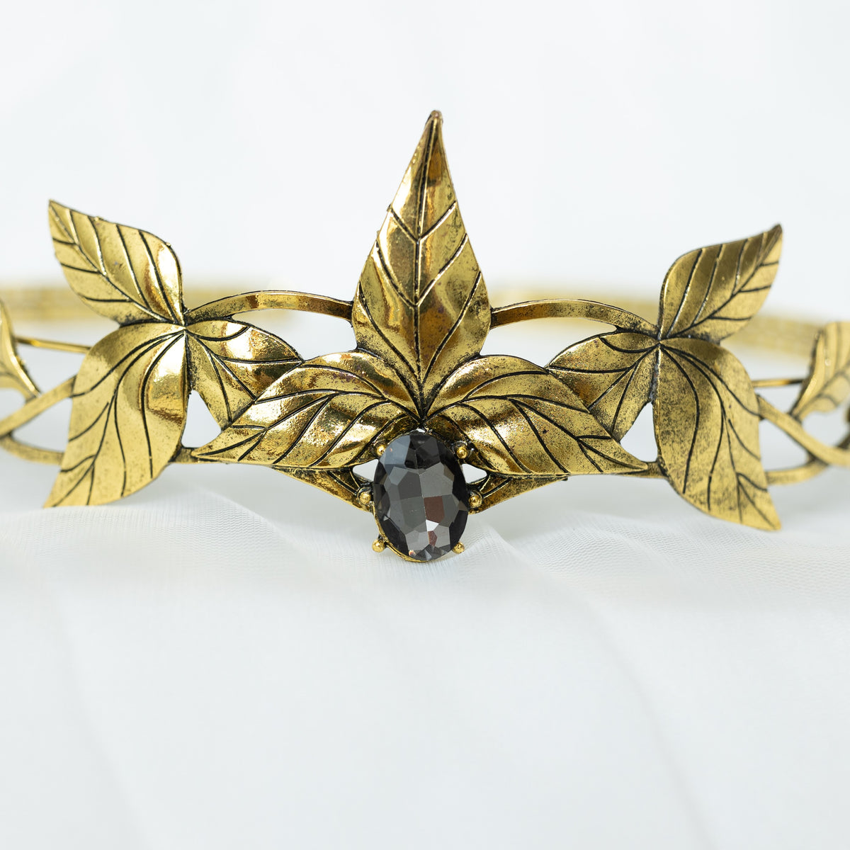 A gray and gold tiara with laurel leaf detailing and a central gray stone, displayed against a white background. Front close up view