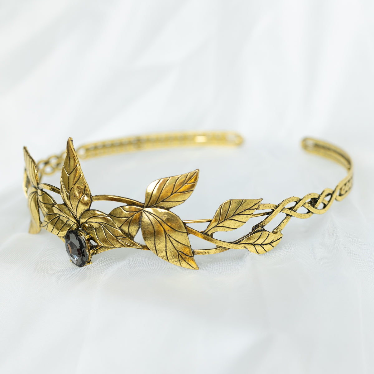 A gray and gold tiara with laurel leaf detailing and a central gray stone, displayed against a white background. Side front view 