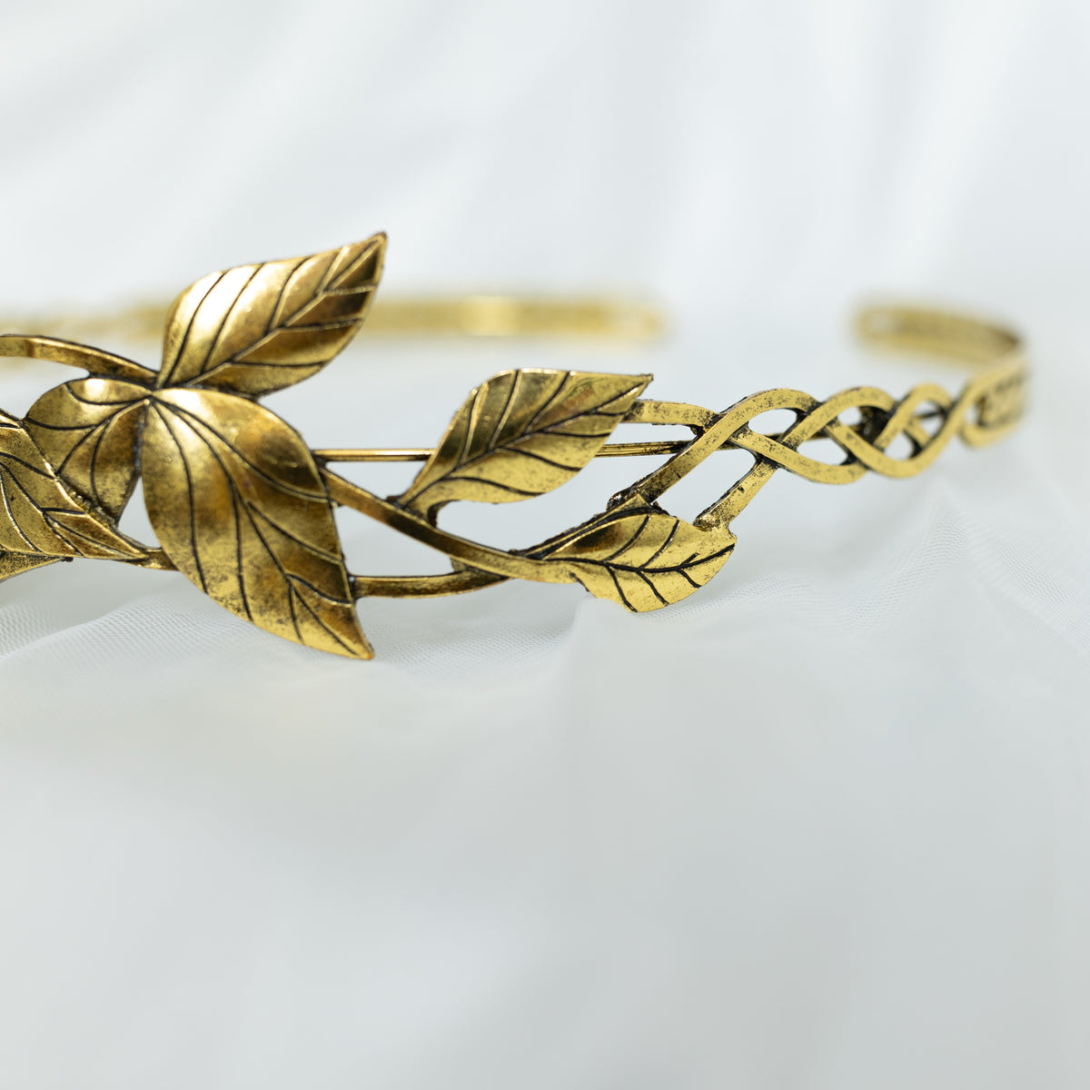 A gray and gold tiara with laurel leaf detailing and a central gray stone, displayed against a white background. Side view 