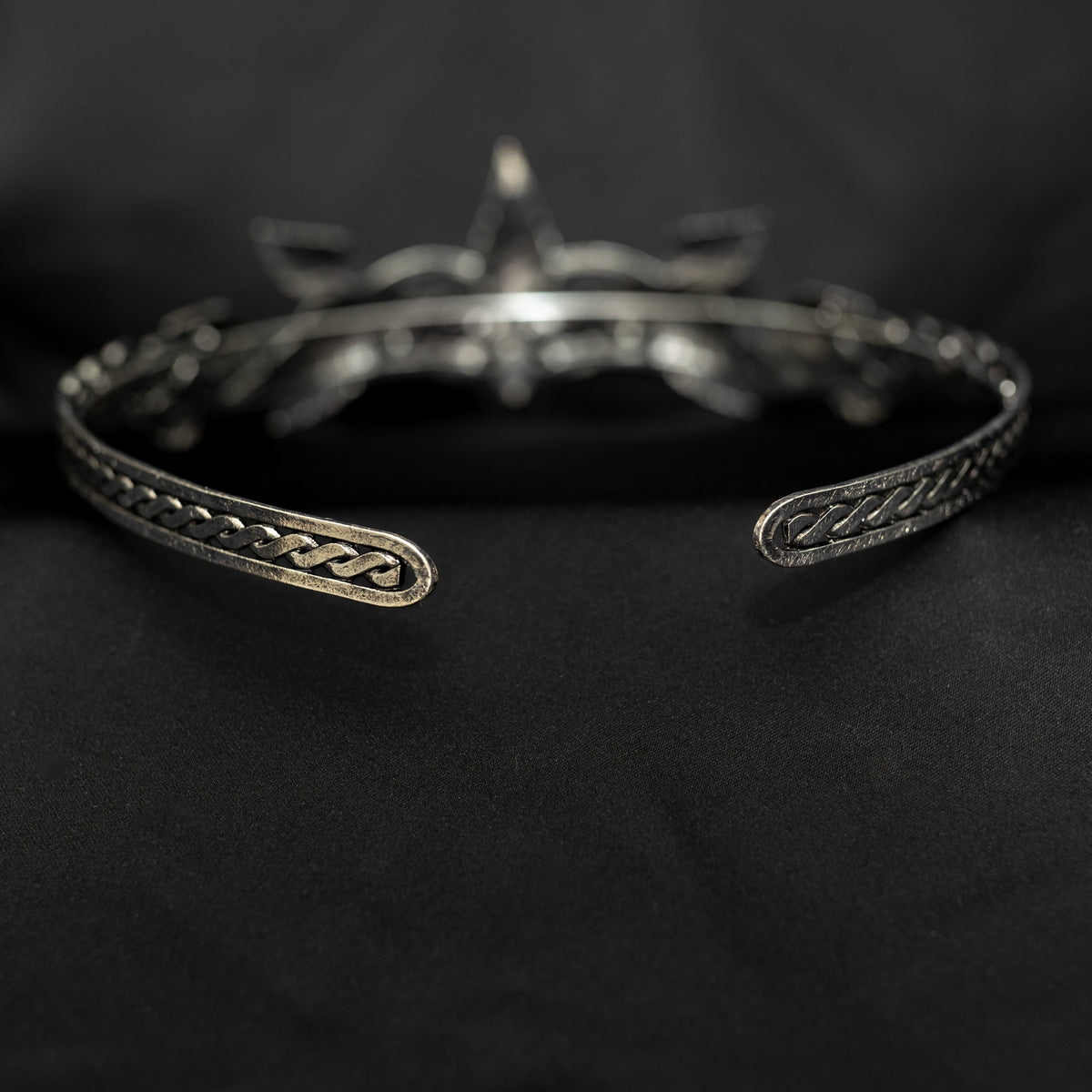 A silver-colored tiara with laurel leaf patterns and a central light green gemstone, displayed against a black background.