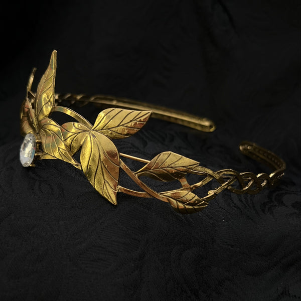 A gold-toned metal hair claw clip decorated with leaf and vine motifs, shown against a textured black fabric background.