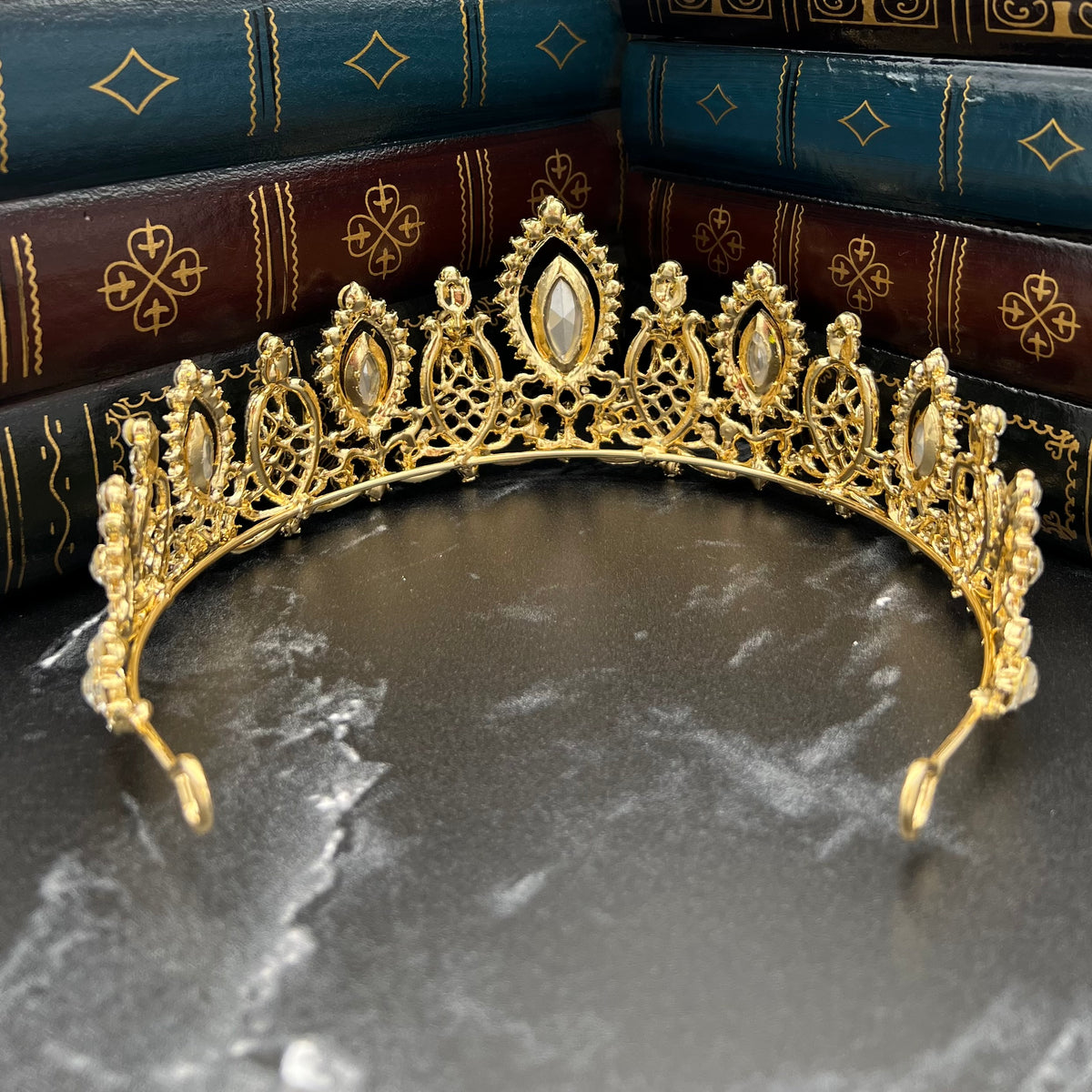Gold tiara on a dark surface with decorative books in the background