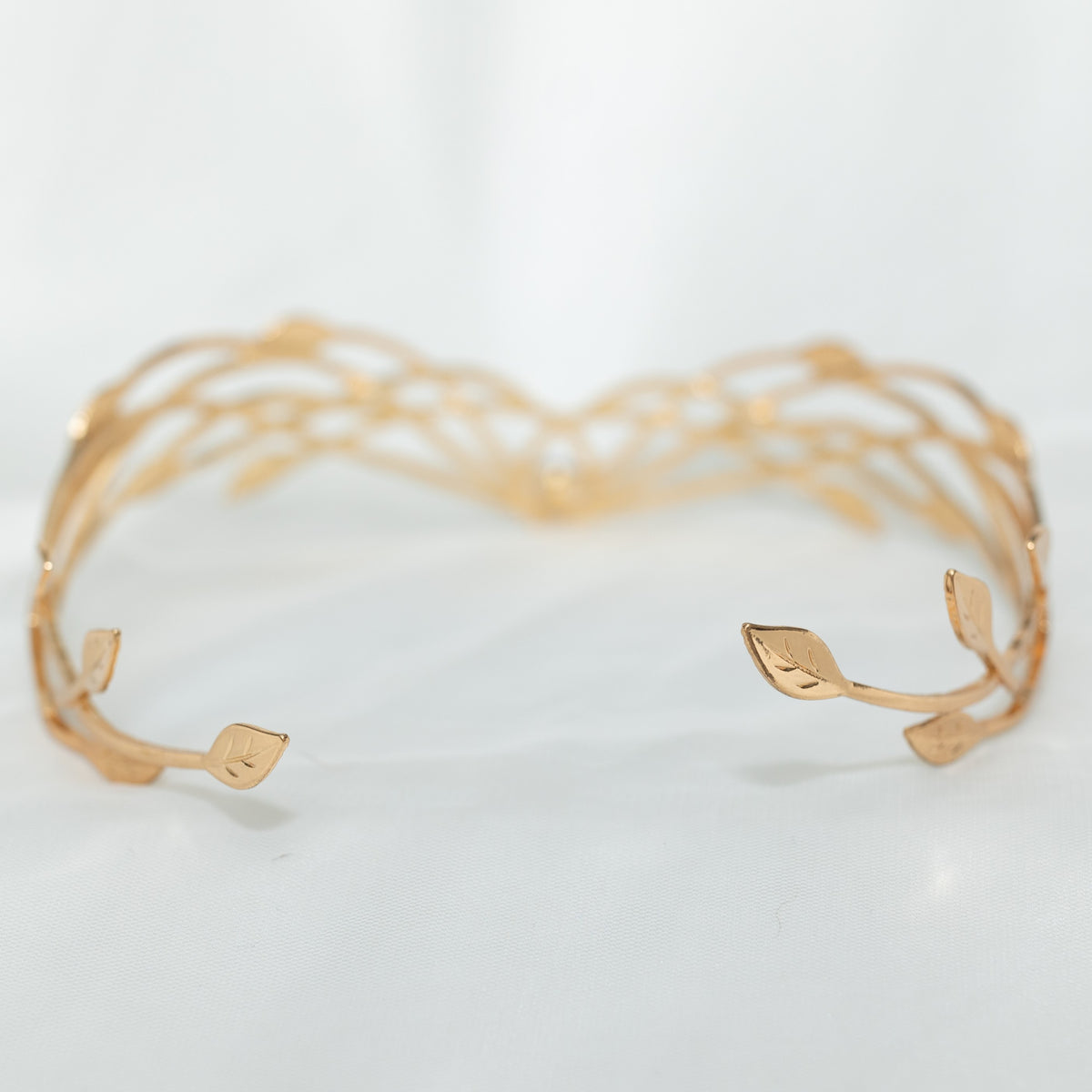 A gold-colored metal crown with a woven design and a central blue crystal, displayed against a white background.