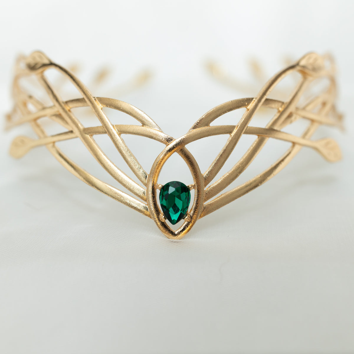Gold tiara  crown with green gemstone on a light background