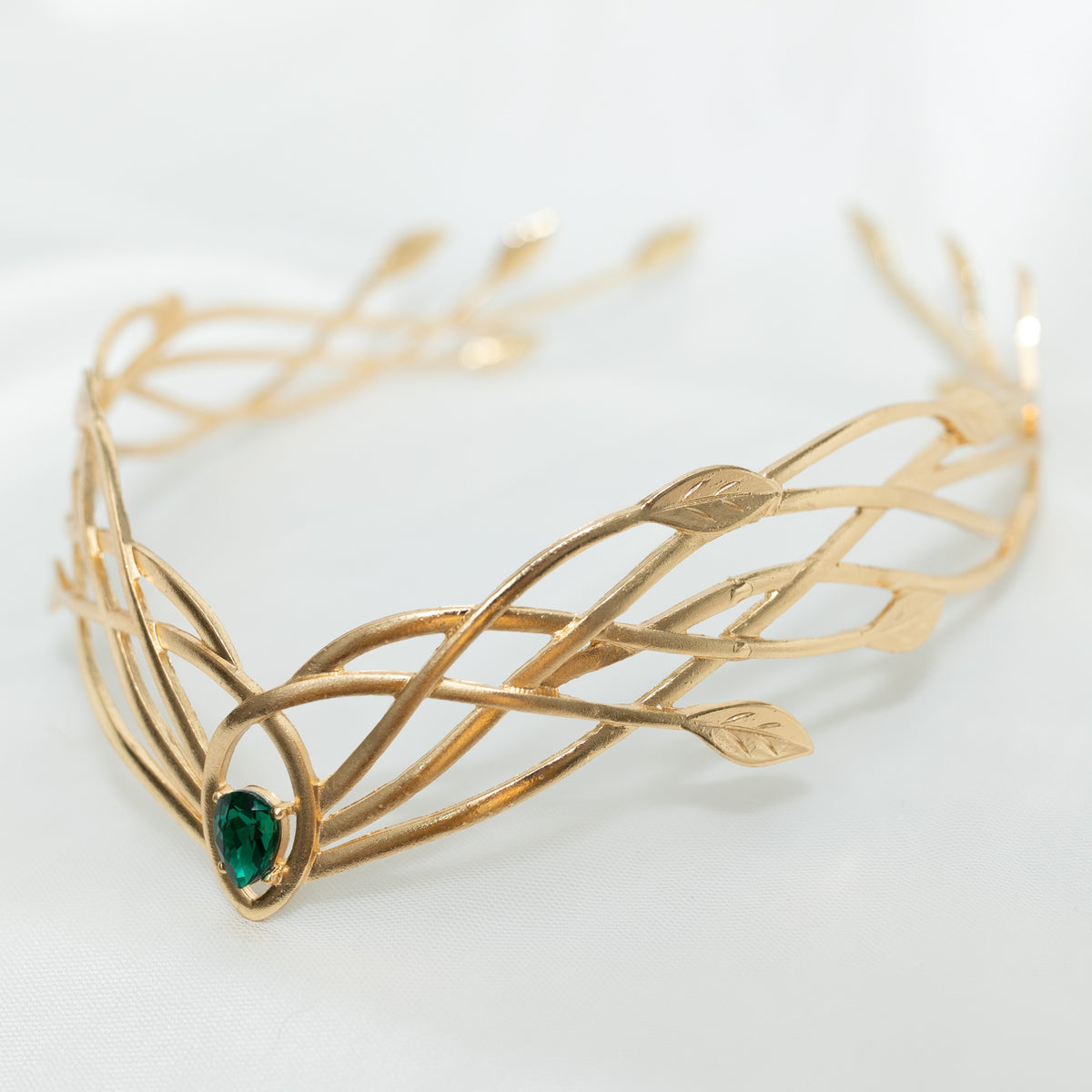 Gold tiara  crown with green gemstone on a light background