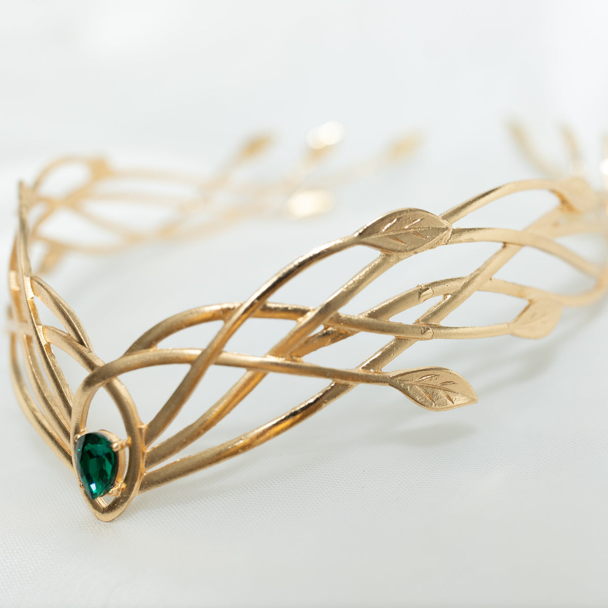 Gold tiara  crown with green gemstone on a light background