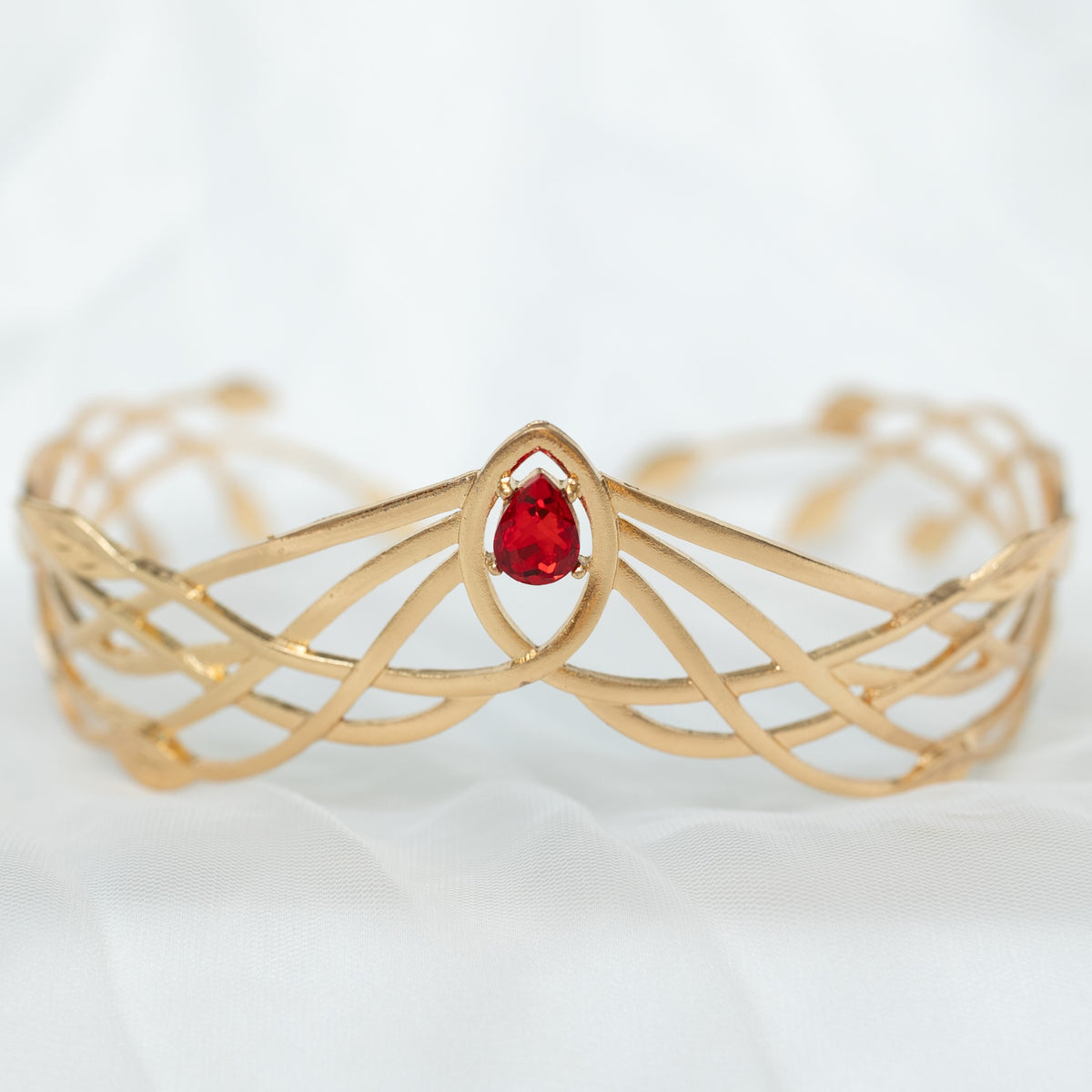 A gold-colored metal crown with a woven design and a central red crystal.