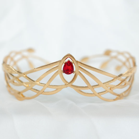 A gold-colored metal crown with a woven design and a central red crystal.