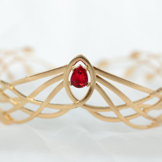 Gold bracelet with a red gemstone on a white background