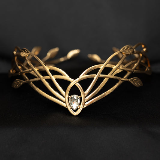 A gold-colored metal crown with a woven design and a central clear crystal, displayed against a black background.
