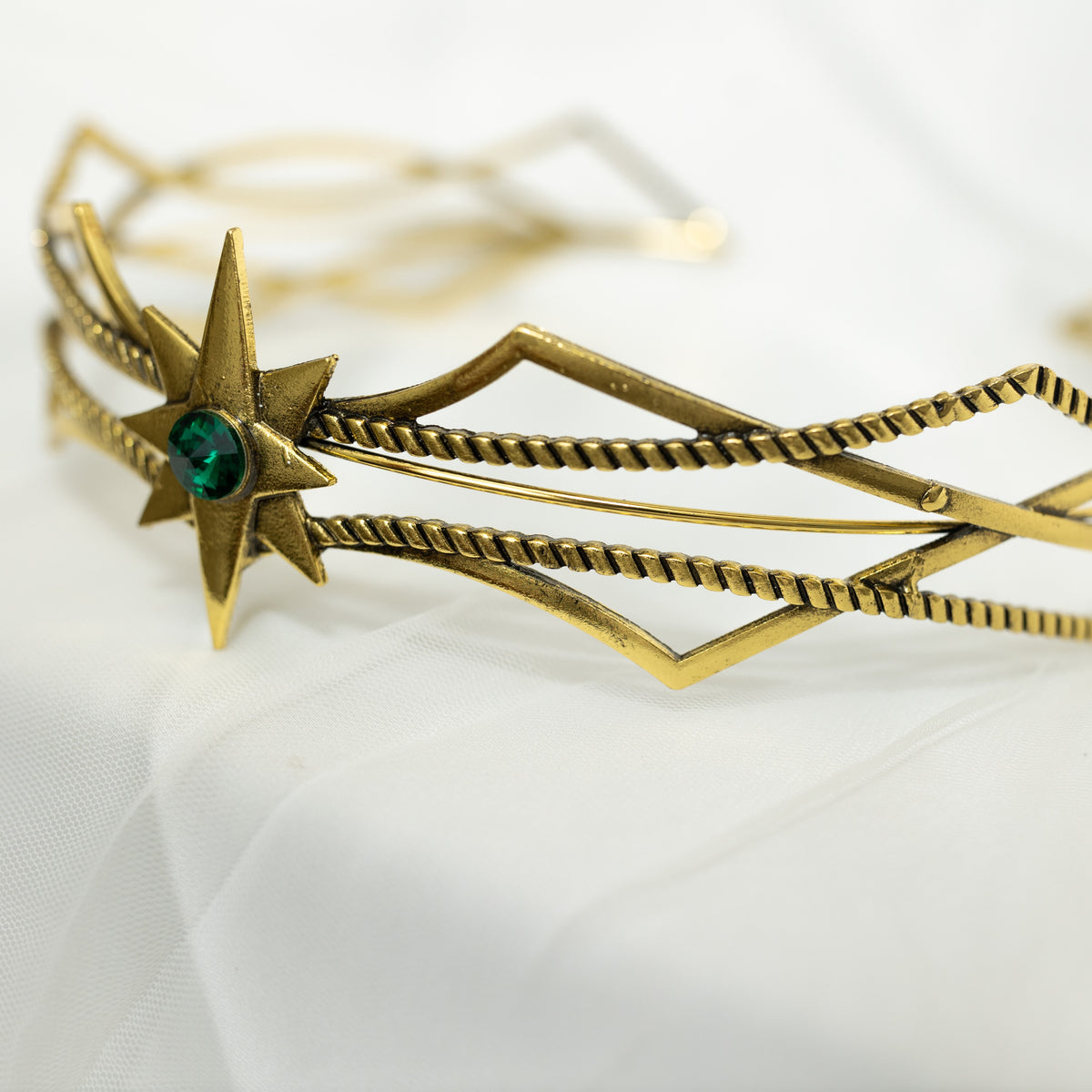 Gold headpiece with star design and green gemstone on a white background