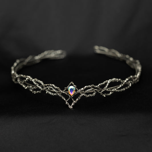 A silver-toned metal cuff bracelet with a twisted, vine-like design and a central iridescent teardrop gemstone, displayed on a dark black background.