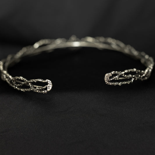 A silver open cuff bracelet with textured, twisted details on both ends, displayed on a dark black background.