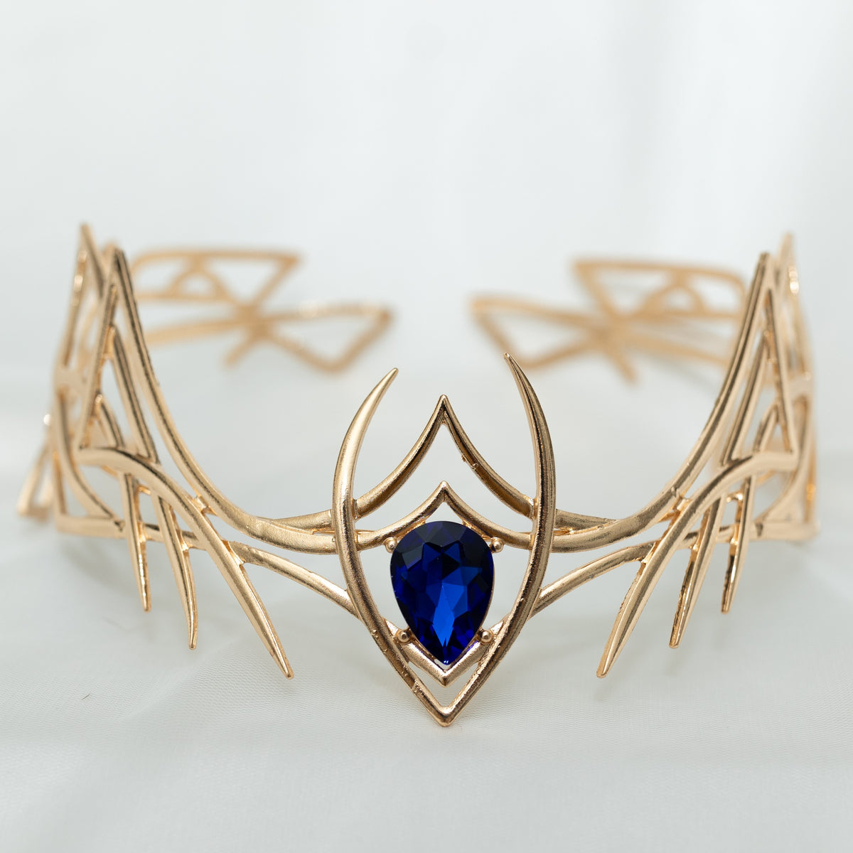 Gold-colored jewelry piece with a blue gemstone on a light gray background