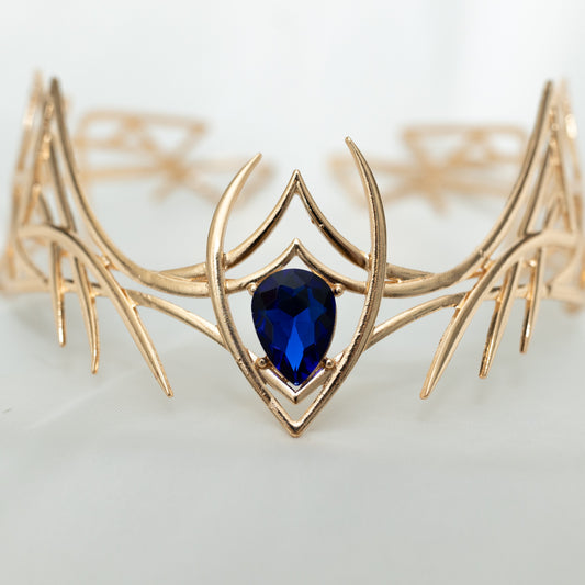 Gold elven-style crown with a blue gemstone on a light gray background